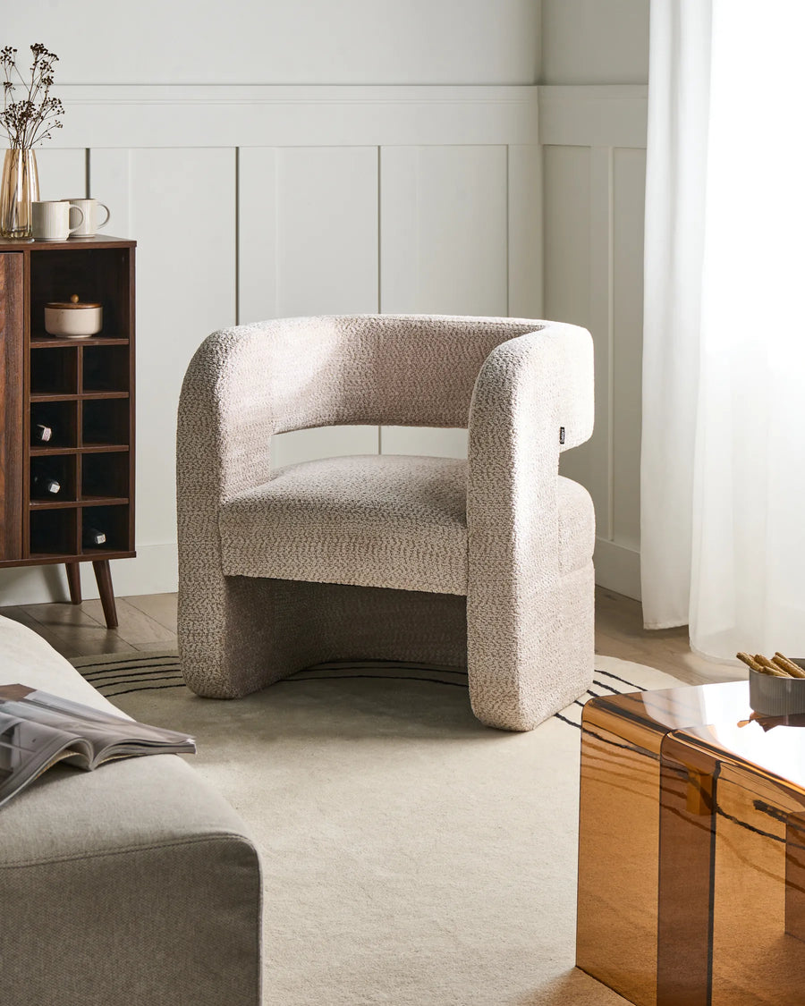 Beige armchair in a modern living room setting with a wooden side table and bookshelf.