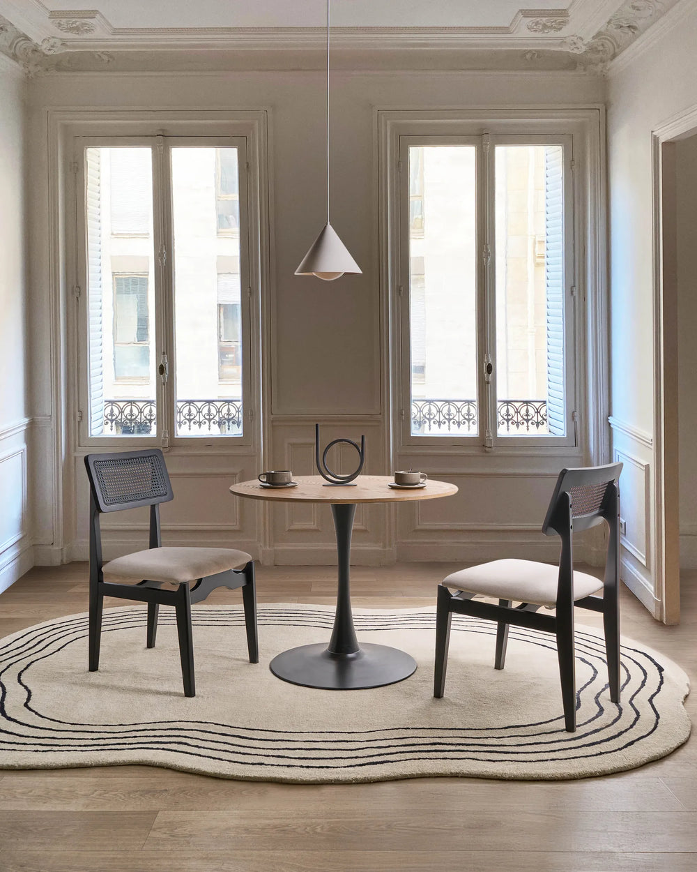 Black cane-back dining chairs styled in an elegant, light-filled dining space with minimalist décor, soft neutral tones, and refined architectural details, creating a modern Parisian and contemporary luxury atmosphere.