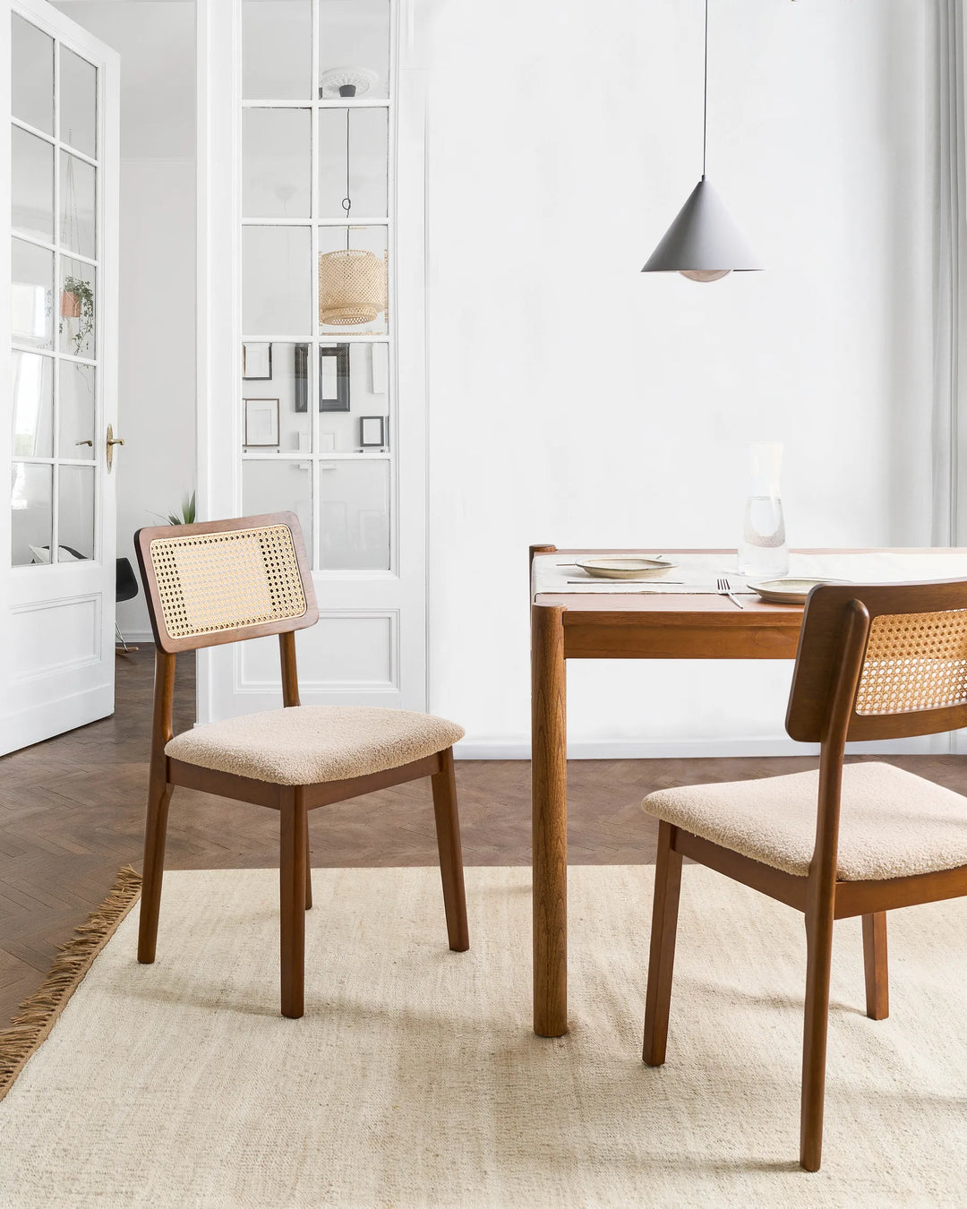 Placed within a bright and elegant dining space, this cane-back dining chair adds warmth, texture, and timeless character to the room. The walnut-toned frame contrasts beautifully with the light boucle seat and woven rattan panel, creating a refined yet relaxed aesthetic. Perfect for everyday dining and entertaining, it brings a touch of organic craftsmanship and modern elegance to any dining setting.