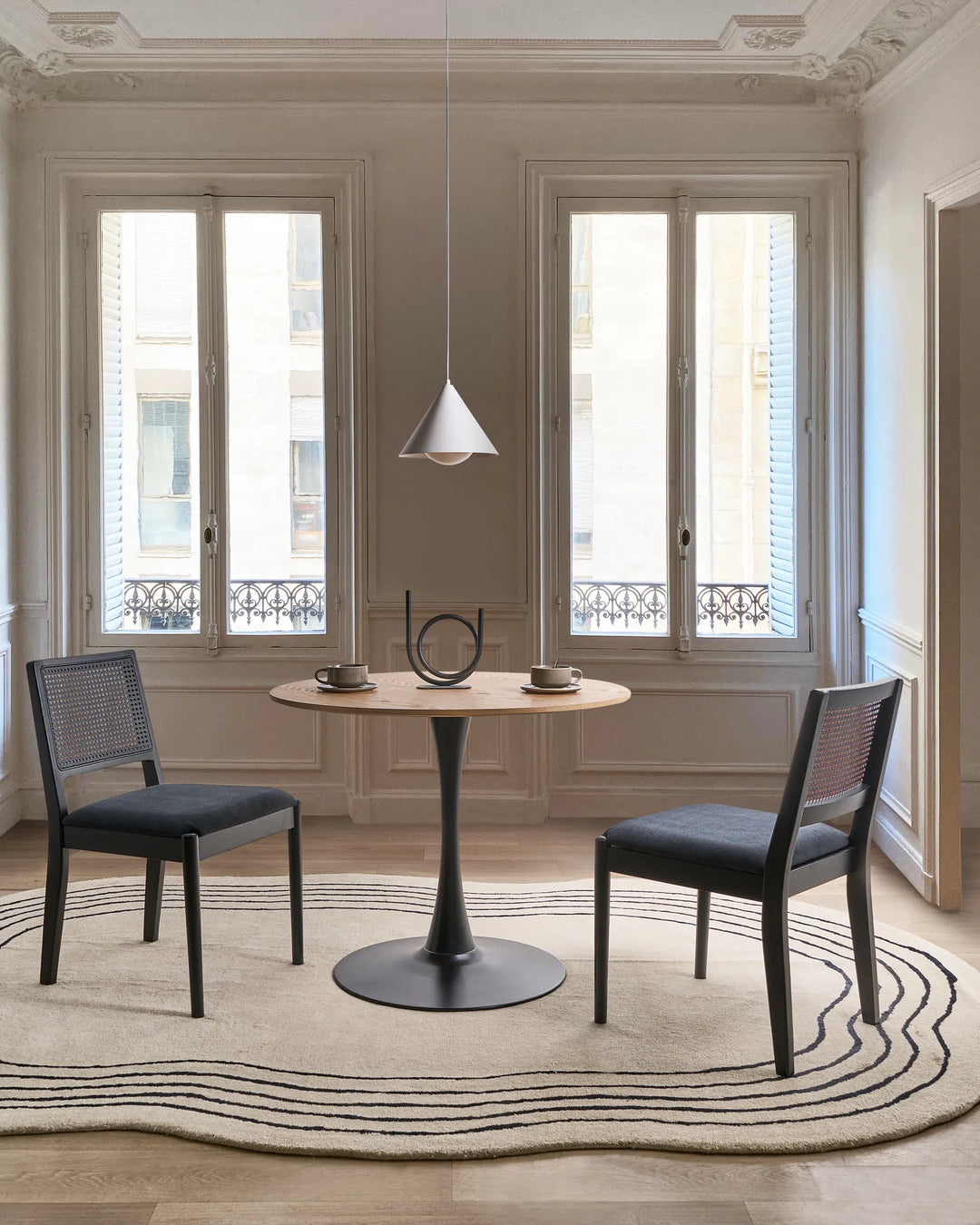 Black cane-back dining chairs styled in a refined, minimalist dining setting with soft neutrals, sculptural decor, and classic architectural details, creating a modern Parisian and contemporary luxury atmosphere.