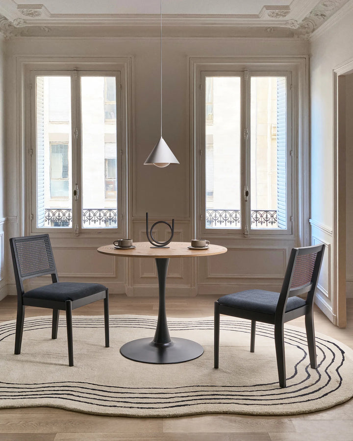 Black cane-back dining chairs styled in a refined, minimalist dining setting with soft neutrals, sculptural decor, and classic architectural details, creating a modern Parisian and contemporary luxury atmosphere.