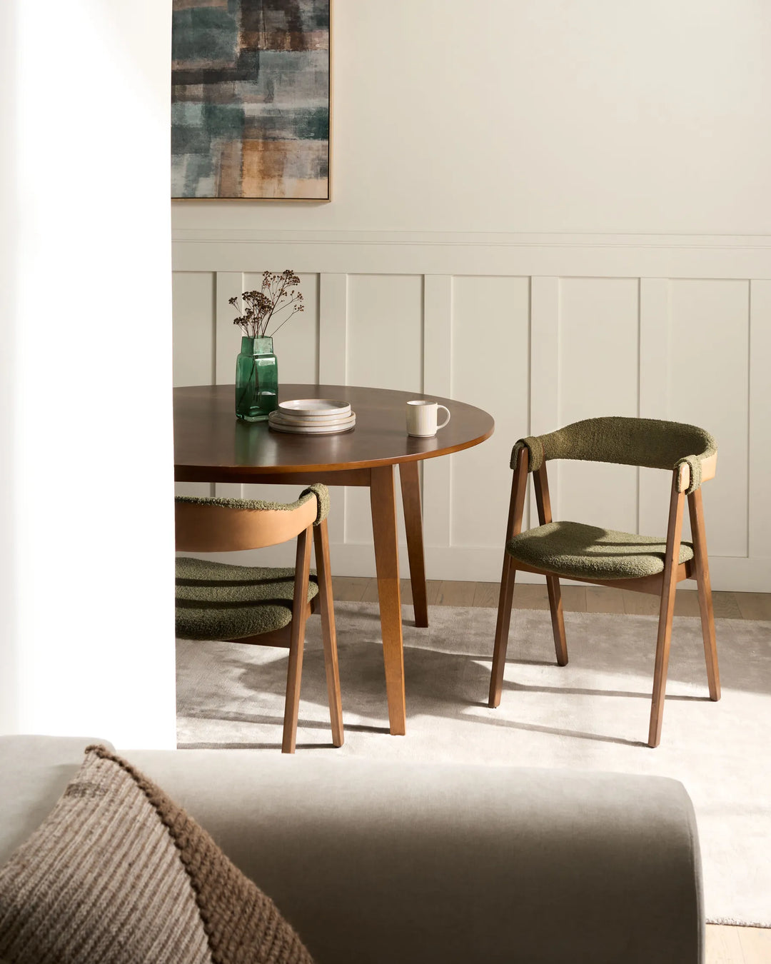 Contemporary dining space featuring olive bouclé chairs and a dark wood round table, creating a warm, organic, and inviting atmosphere.