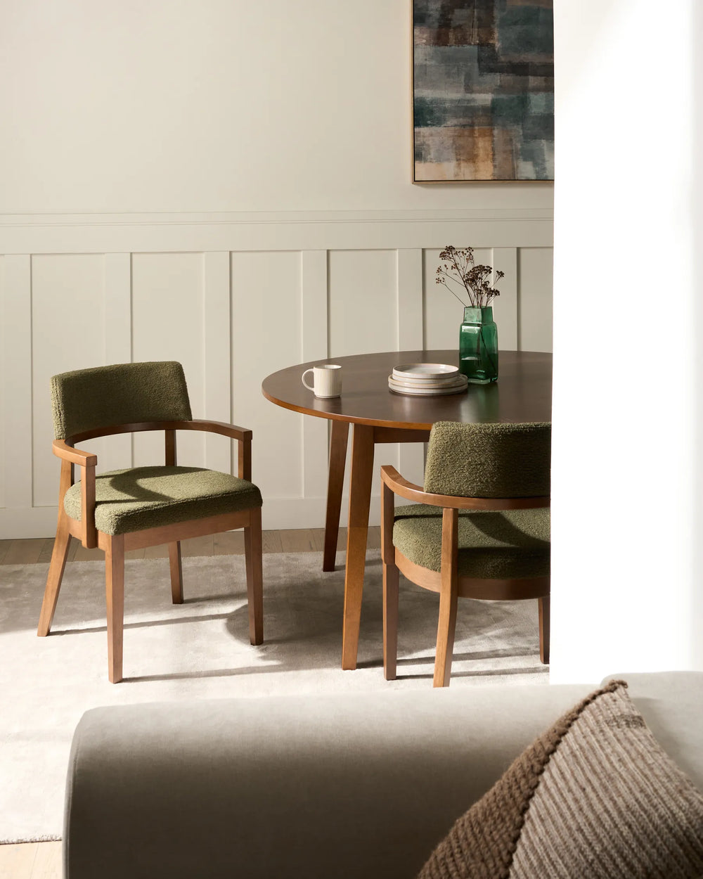 Cozy dining area featuring olive-green bouclé chairs and a dark wood table, creating a warm and modern atmosphere.