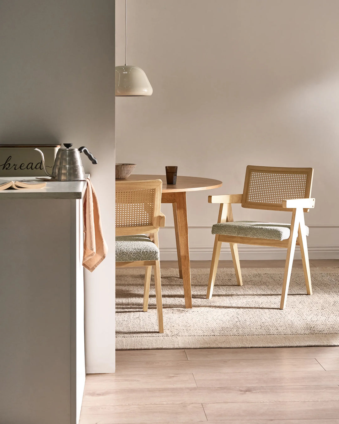Light wood dining chairs with woven cane backrests and grey boucle seats around a wooden dining table in a modern dining room.
