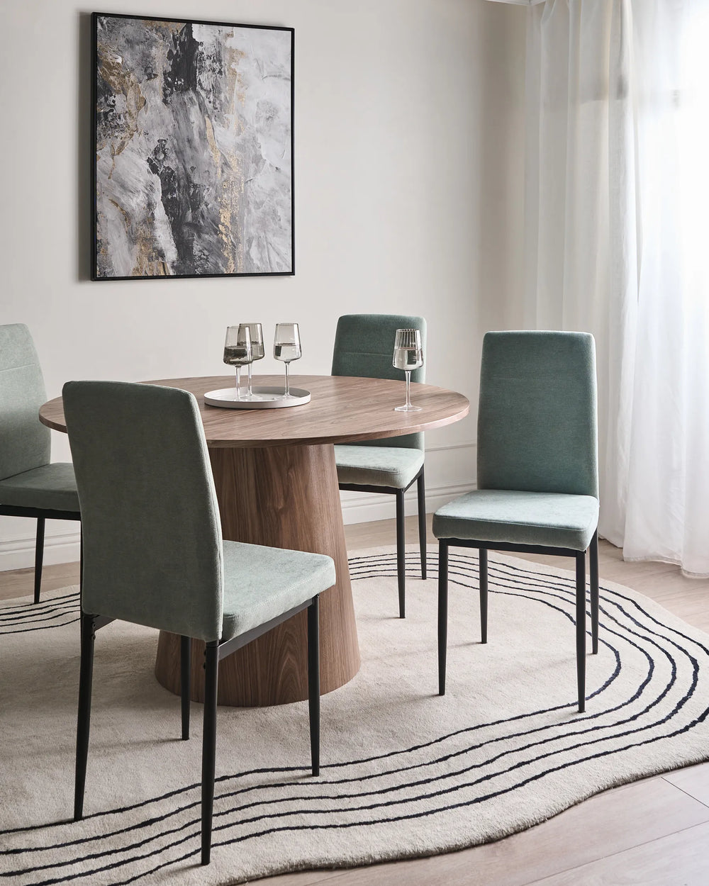Light green dining chairs around a round wood table in a bright, modern dining room with neutral décor.