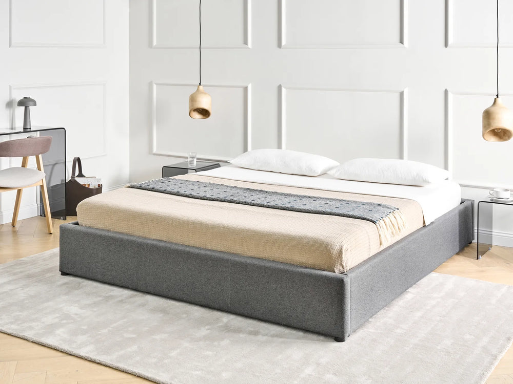 Gray upholstered bed in a modern bedroom setting with white walls and minimal decor.