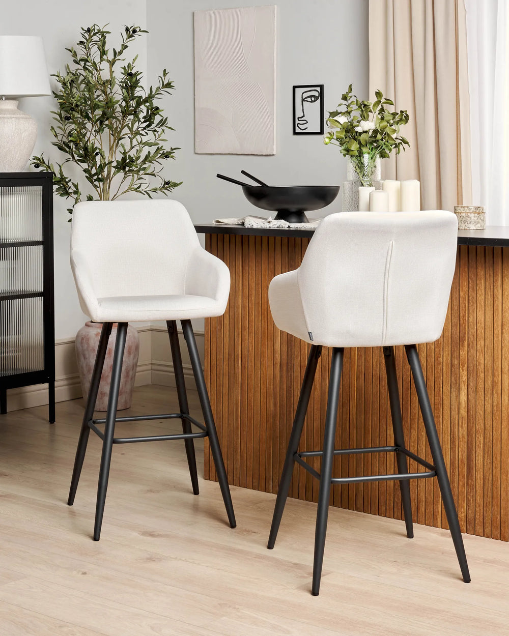 Off-white velvet bar chairs with rounded backrests and slanted black metal legs around a bar counter in a contemporary kitchen or dining space with modern décor.