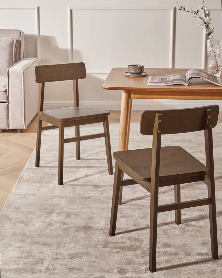 Dark wood dining chairs styled around a wooden dining table in a warm, cozy dining room with soft neutral tones, a textured rug, natural lighting, and simple tabletop décor.