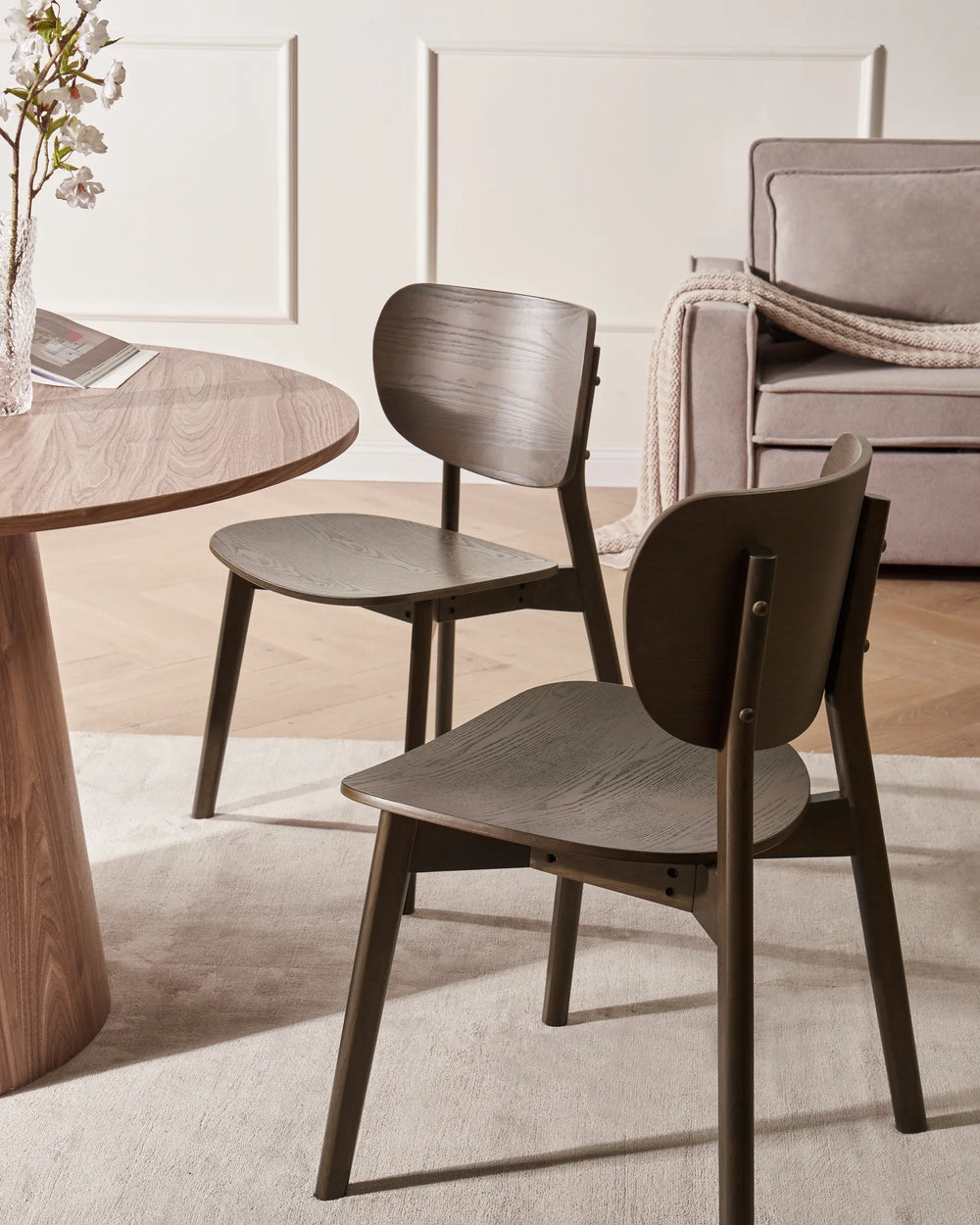 Contemporary wooden dining chairs styled in a cozy neutral dining space with a round wood table, soft textures, warm lighting, and minimalist décor, creating a modern organic and Scandinavian-inspired ambiance.