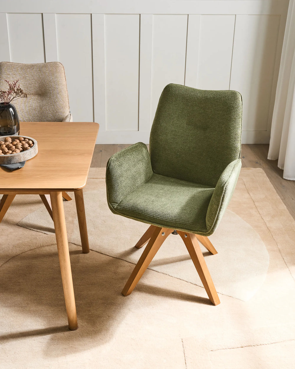 Green faux linen swivel dining chairs with oak legs around a dining table in a bright, Scandinavian-style dining space.
