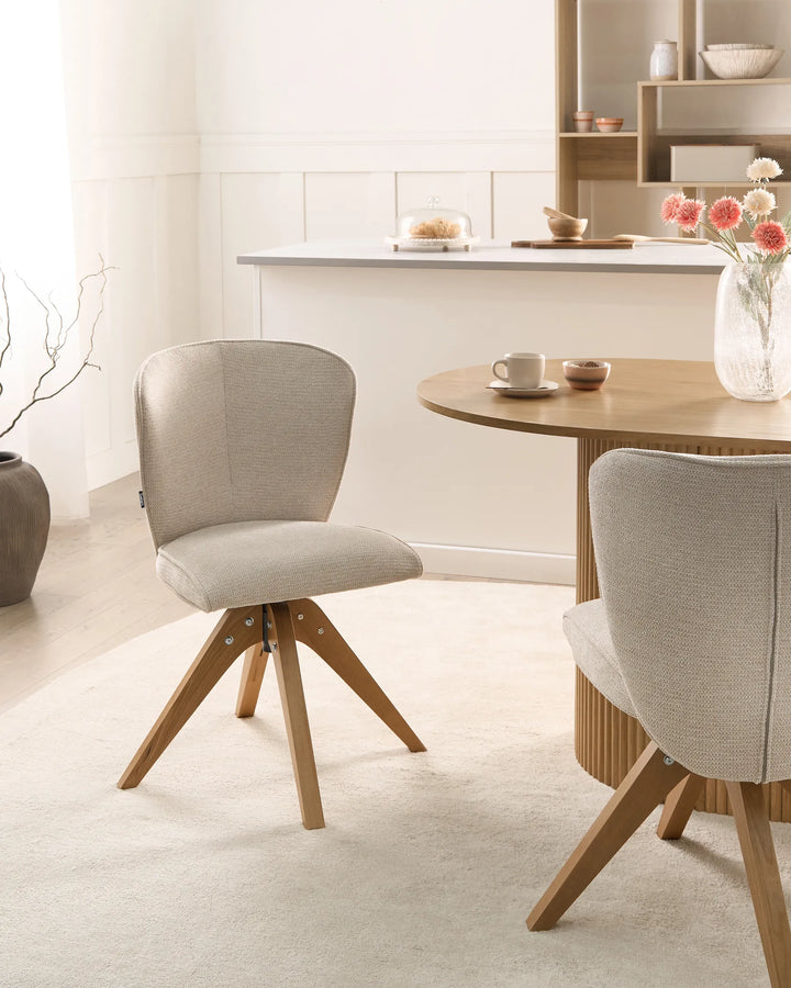 Light beige fabric swivel dining chairs with wooden legs arranged around a dining table in a bright, modern dining space with minimalist décor.