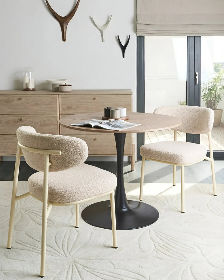 Light beige bouclé dining chairs with rounded backrests and metal legs arranged around a dining table in a bright, modern dining space with minimalist décor.
