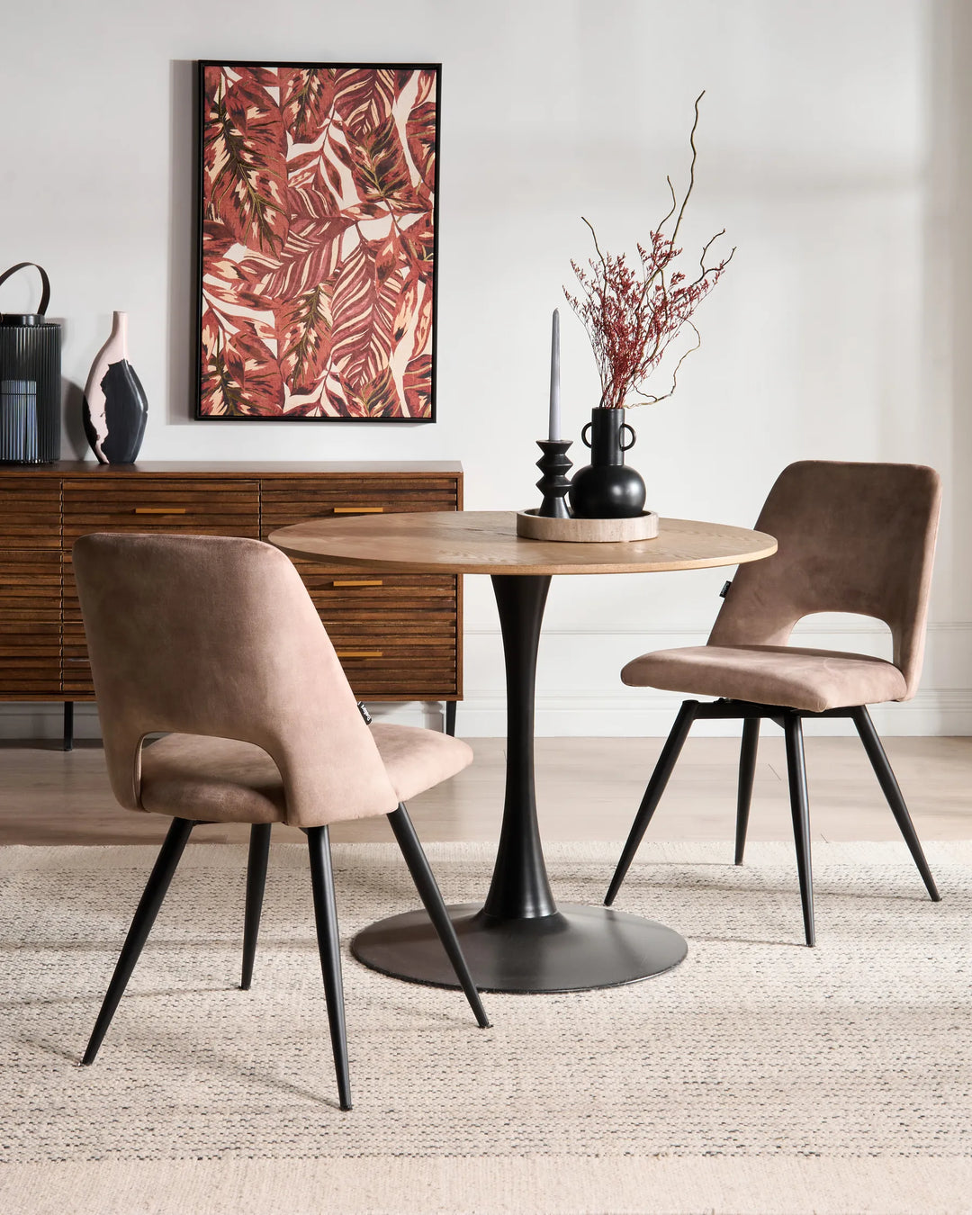 Taupe dining chairs around a round wood table in a warm, modern dining space with black accents and botanical artwork.