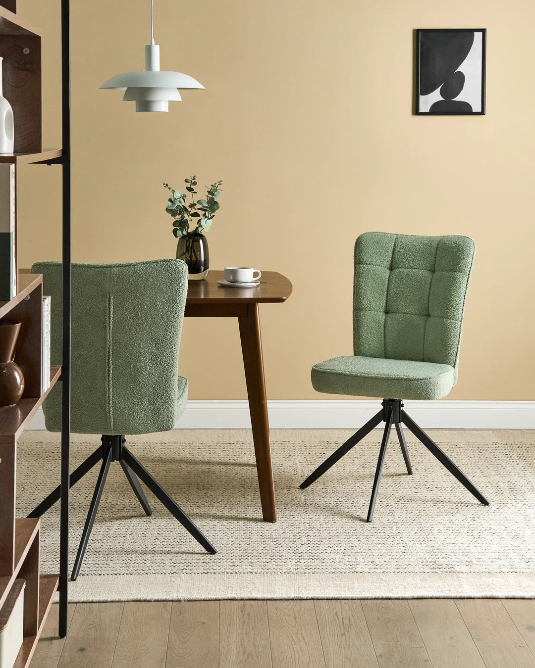 Light green bouclé swivel dining chairs around a walnut dining table with a vase, coffee cup, pendant light, shelving, and a cream rug.