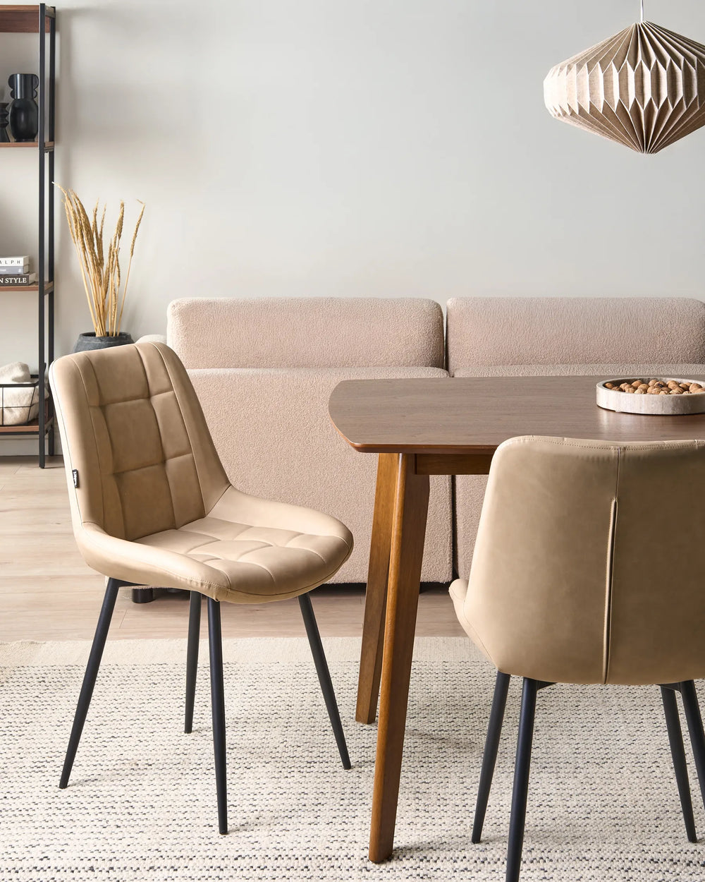 Beige faux leather dining chairs styled around a wooden dining table in a warm contemporary dining space with a textured rug, neutral sofa, shelving, and soft decorative lighting.
