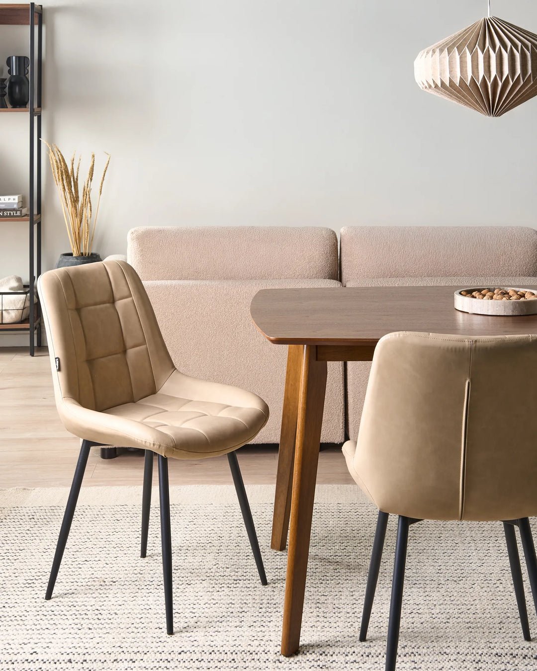 Beige faux leather dining chairs styled around a wooden dining table in a warm contemporary dining space with a textured rug, neutral sofa, shelving, and soft decorative lighting.