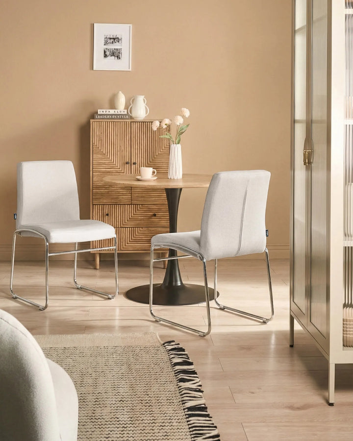 Light grey fabric dining chairs with chrome legs arranged around a dining table in a contemporary dining space with minimalist décor.