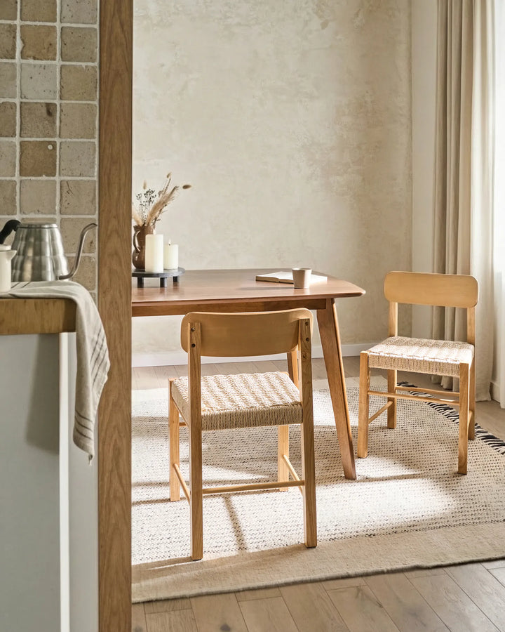 Natural wood woven dining chairs styled in a bright, cozy dining space with soft textures and warm neutral tones, creating an airy, inviting, and relaxed atmosphere.