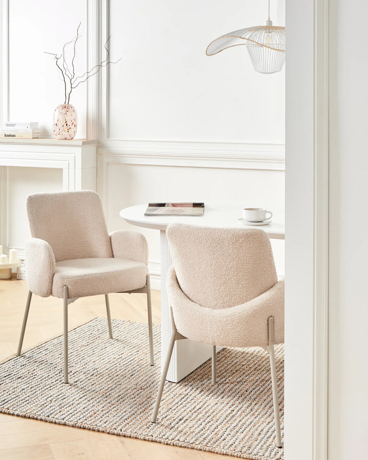 Bright Scandinavian-inspired dining space showcasing cream bouclé armchairs around a white table, complemented by soft neutral tones, textured textiles, and minimalist décor for a warm and inviting atmosphere.