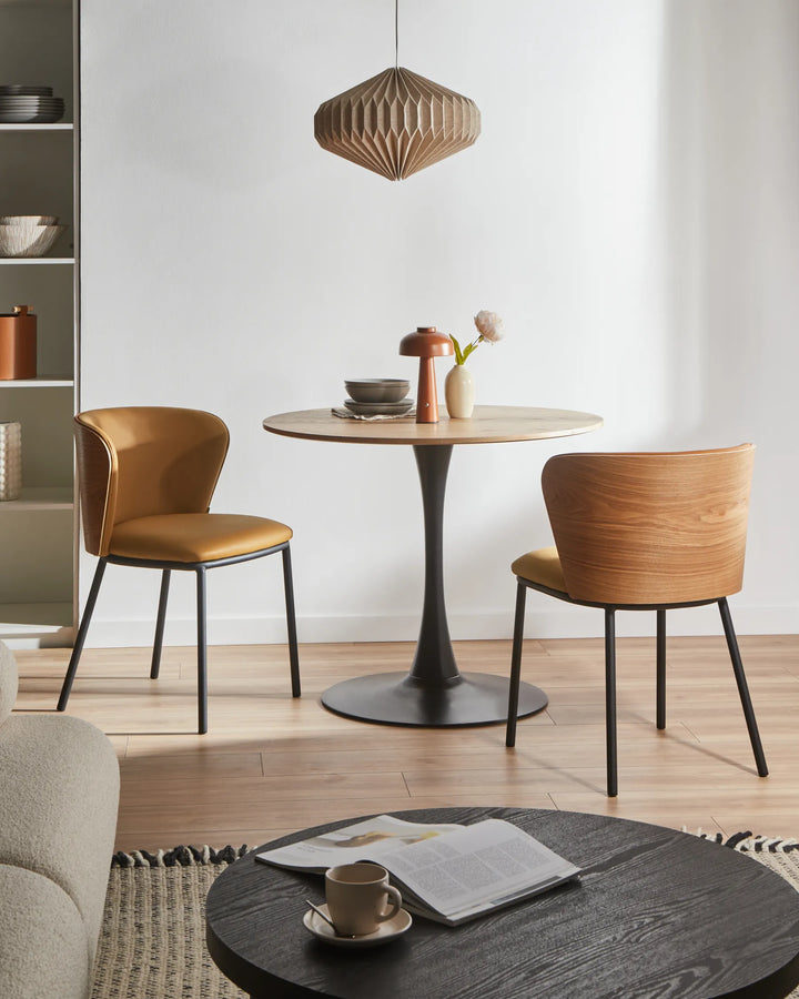 Modern Scandinavian-style dining setting showcasing the chair’s camel faux leather upholstery, natural wood veneer back, and minimalist black metal frame, creating a warm and inviting atmosphere.