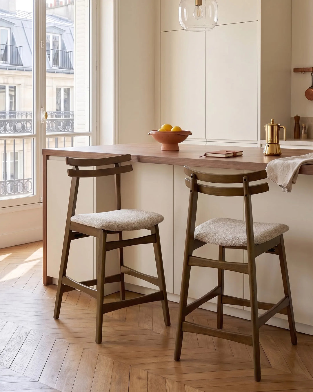 Positioned around a modern kitchen island, these upholstered bar chairs add warmth and sophistication to the interior. The dark wood finish contrasts beautifully with the light cabinetry and neutral textiles, creating an inviting space for casual meals, entertaining guests, or everyday gatherings.