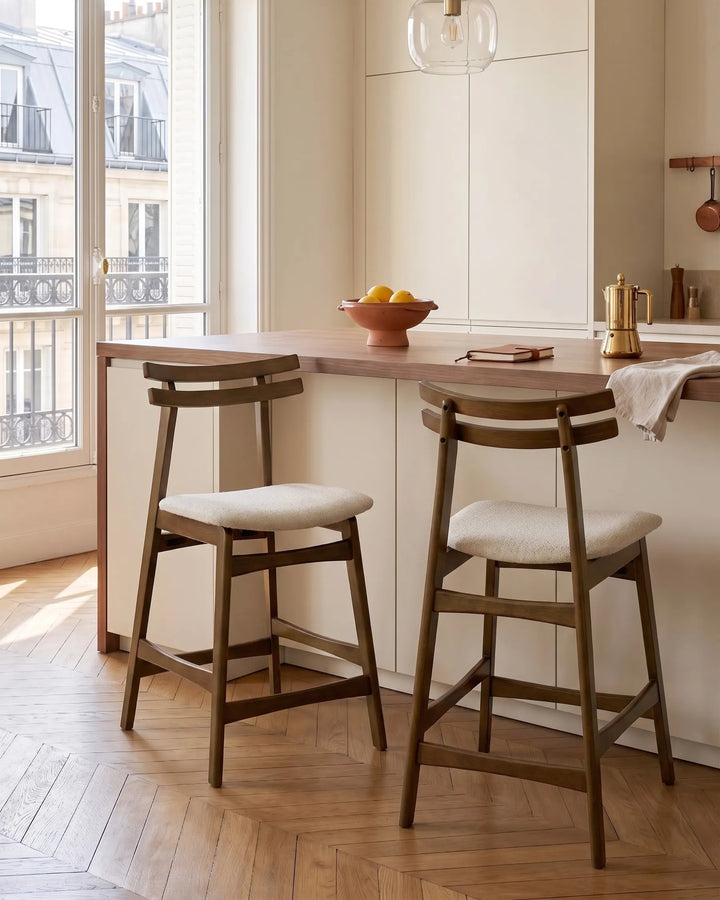 Set around a contemporary kitchen island, these upholstered bar chairs bring warmth, texture, and refined elegance to the space. The rich wood finish pairs beautifully with soft neutral tones, creating an inviting atmosphere ideal for casual dining, entertaining, or morning coffee.