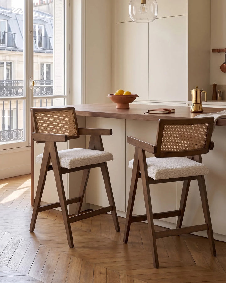 Dark wood bar chairs with woven cane backrests and cream upholstered seats at a kitchen island in a modern kitchen.