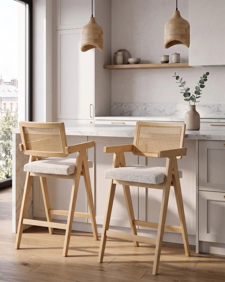 Light wood bar chairs with woven cane backrests and cream upholstered seats at a kitchen island in a bright modern kitchen.