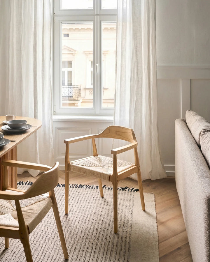 Light wood woven armchairs styled in a soft, Scandinavian-inspired dining space with neutral tones, sheer curtains, natural textures, and warm minimalist décor.
