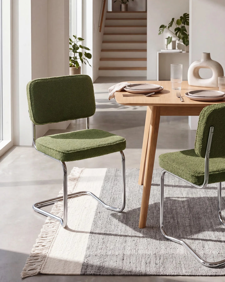 Green bouclé cantilever dining chairs with silver metal frames arranged around a dining table in a bright, modern dining space with minimalist décor.