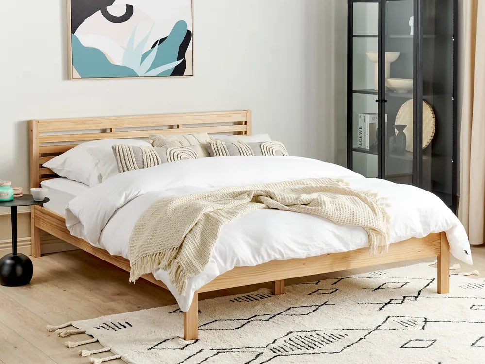 Light brown pine wood bed frame in a simple bedroom setting with a neutral wall, soft bedding, and minimal decor in the background.