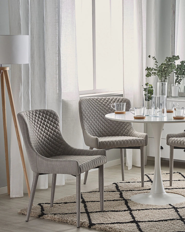 Light Grey quilted dining chairs paired with a glass-top table in a stylish modern dining room.