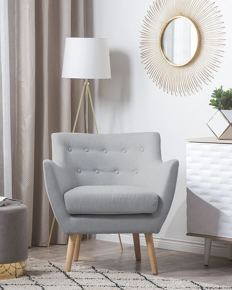 Gray armchair in a living room setting with a lamp, mirror, and decor items.