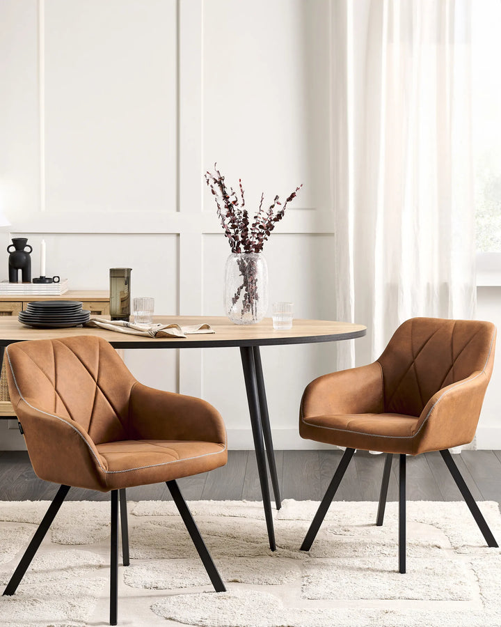 Stylish dining space with matching cognac-brown armchairs around a light wood table, complemented by black metal accents, soft neutral textiles, and elegant decorative accessories.