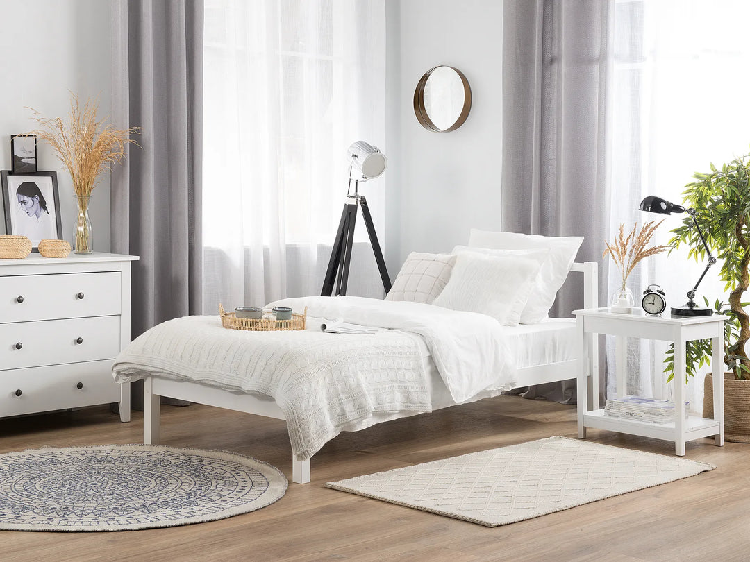 White pine wood bed frame with a simple design, placed in a bright minimalist bedroom with neutral decor in the background.