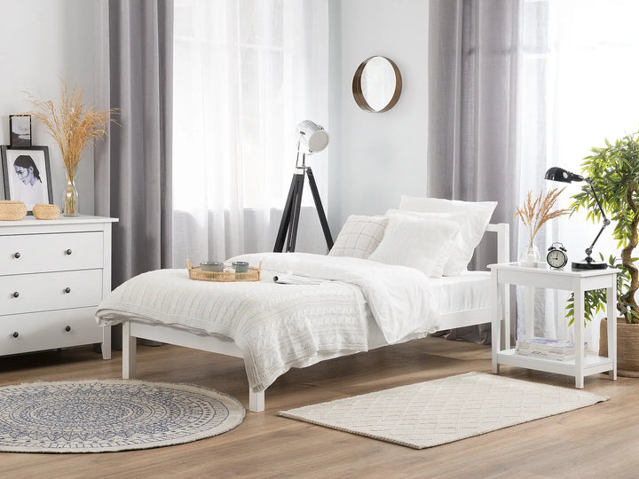 White pine wood bed frame with a simple design, placed in a bright minimalist bedroom with neutral decor in the background.