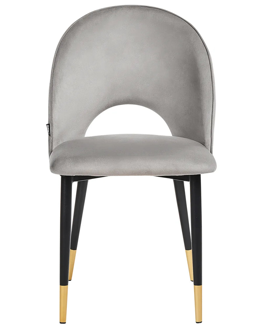 Light grey velvet dining chair featuring a curved open-back silhouette, plush padded seat, and sleek black metal legs with elegant gold-tipped accents.