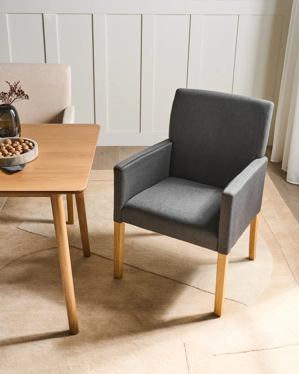 Modern grey armchair styled beside a wooden dining table, creating a warm and inviting dining setting.