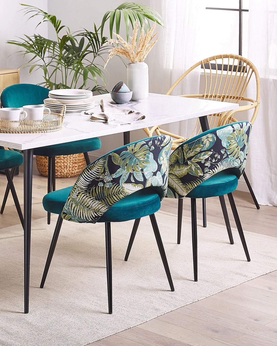 Teal velvet dining chairs with tropical print backs around a white dining table.
