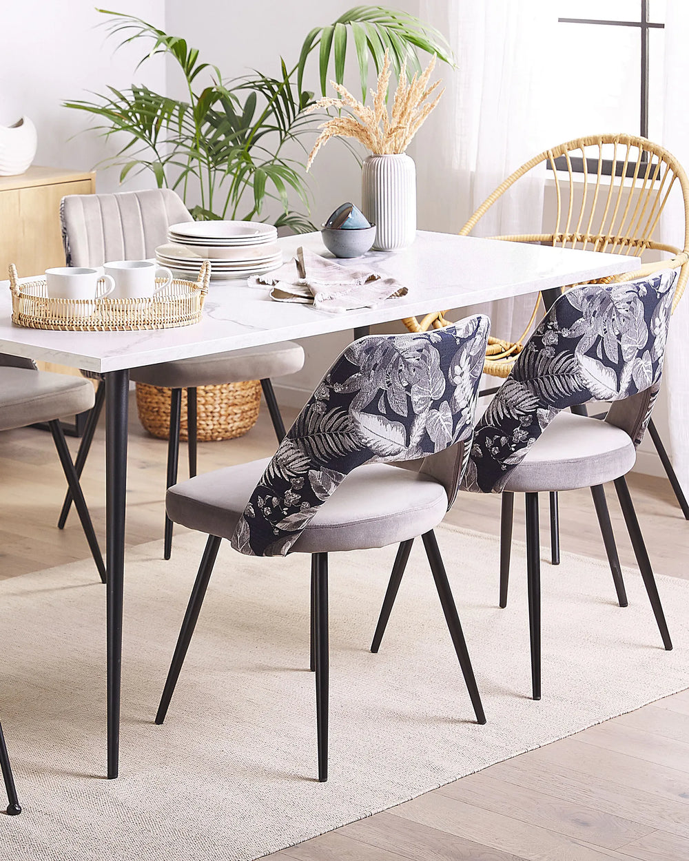 Grey dining chairs with floral-patterned backs around a white dining table in a bright, modern dining room with greenery, rattan accents, and natural light.
