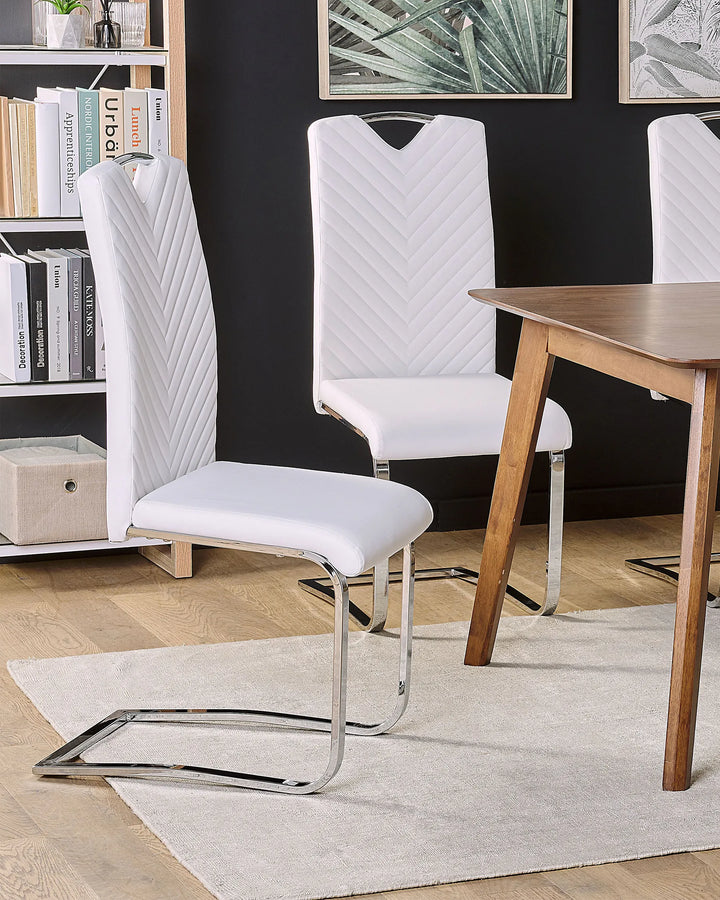 White faux leather cantilever dining chairs styled around a wooden dining table in a contemporary dining room with a black accent wall, botanical wall art, open shelving, light wood flooring, and a soft neutral area rug.