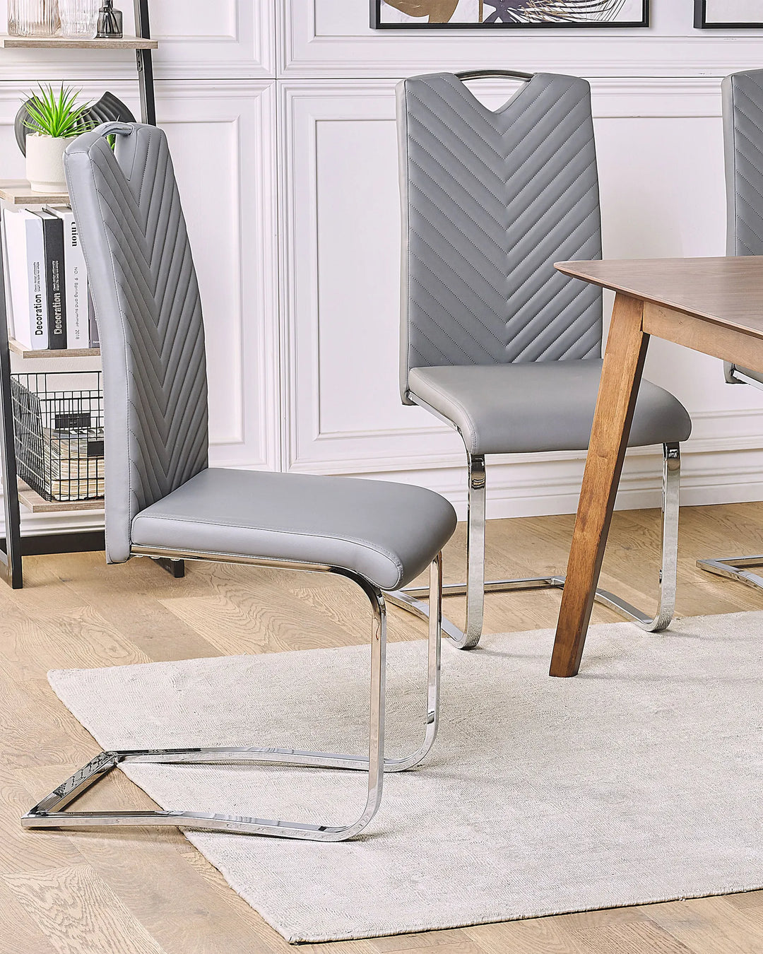 Light grey cantilever dining chairs styled around a wooden dining table in a modern dining room with wall panelling, shelving, oak flooring, and a neutral rug.