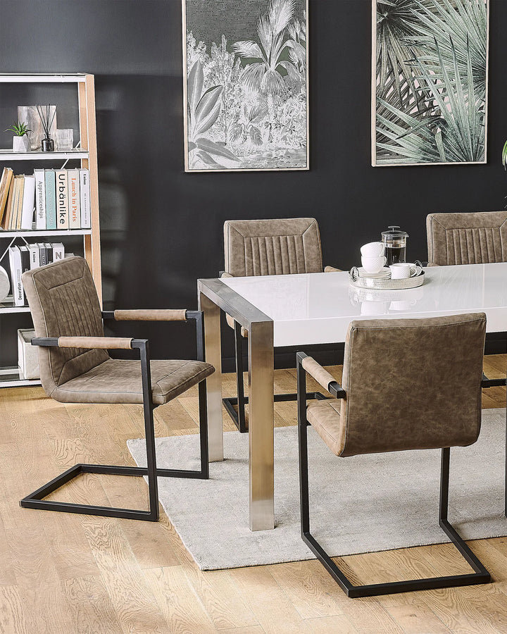Brown dining chairs arranged around a glossy white dining table on a light rug, set against dark accent walls with botanical artwork, open shelving, and modern décor.