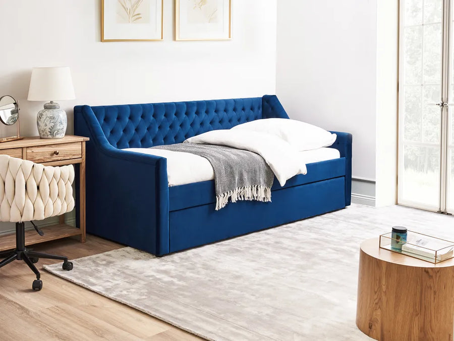 Blue upholstered bed in a room with a wooden side table and white walls.