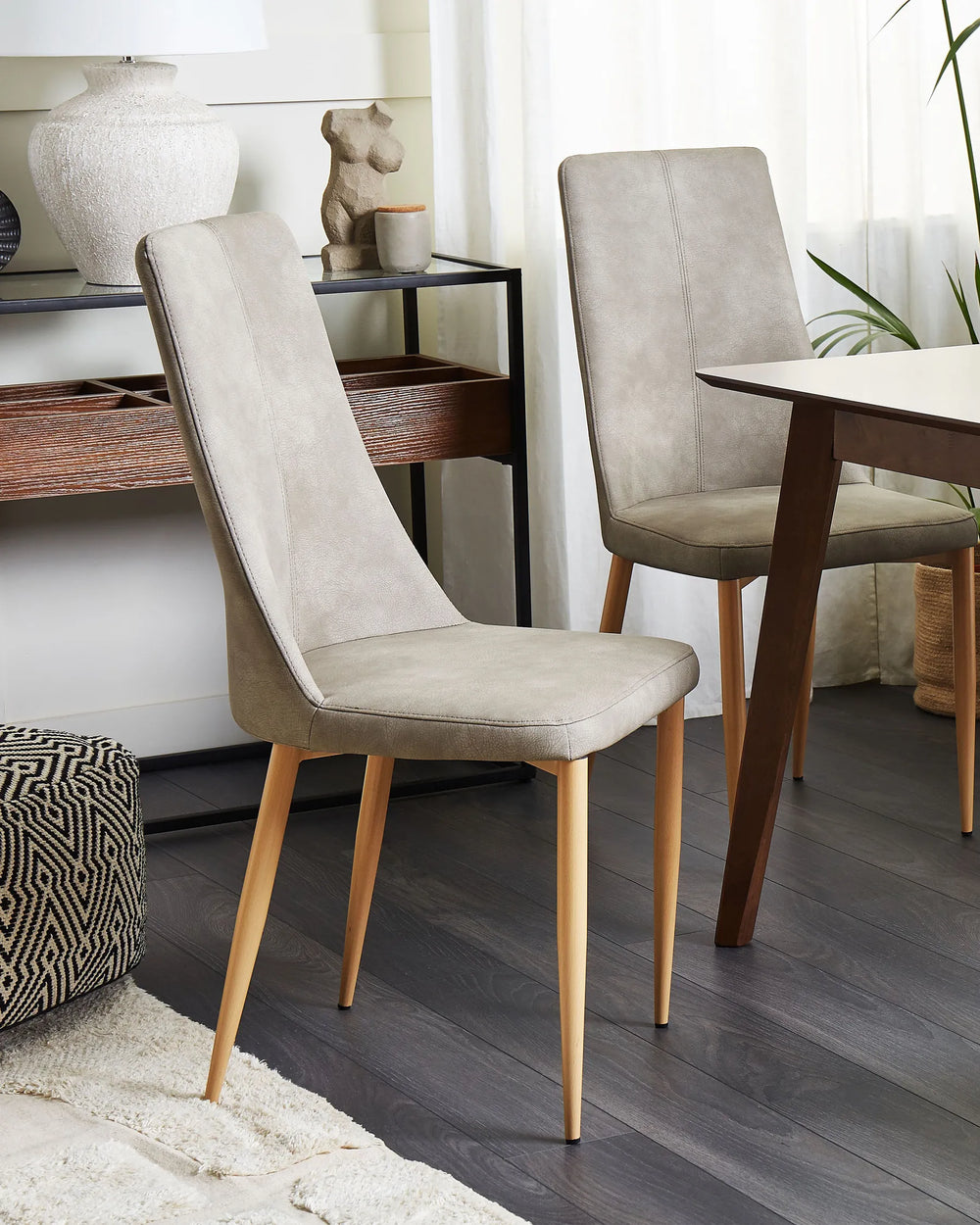 Styled in a modern dining setting, these light grey upholstered chairs bring a refined and inviting look to the space. The combination of textured faux leather, warm wooden legs, and minimalist design complements contemporary, Scandinavian, and transitional interiors.