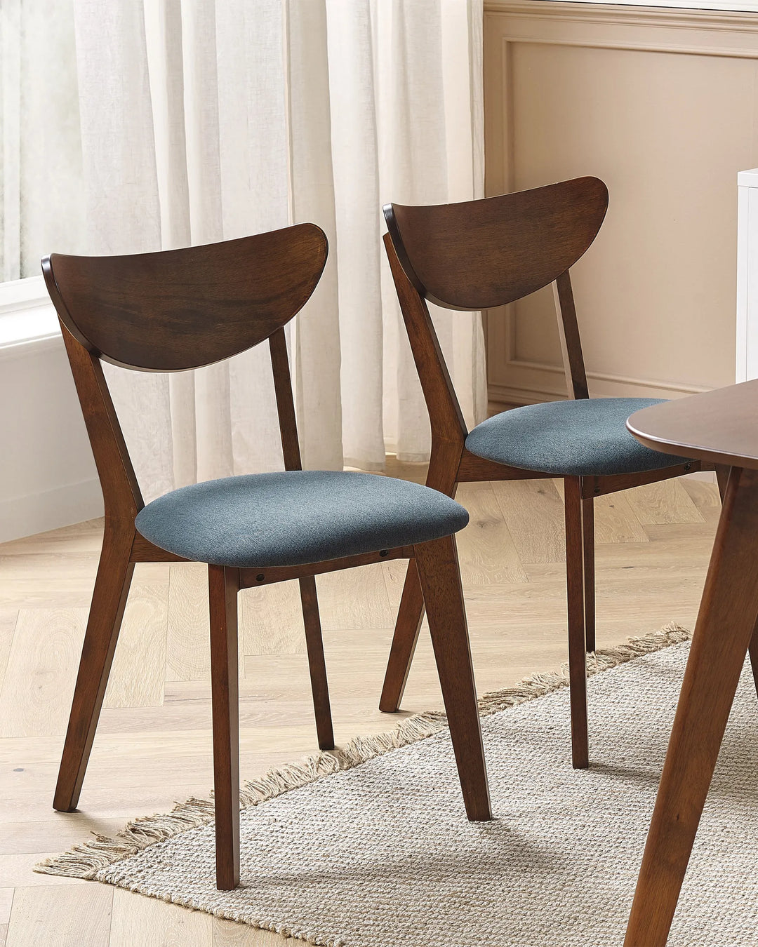 Dark wood dining chairs with curved backrests and upholstered seats styled around a dining table in a warm, modern dining room setting.