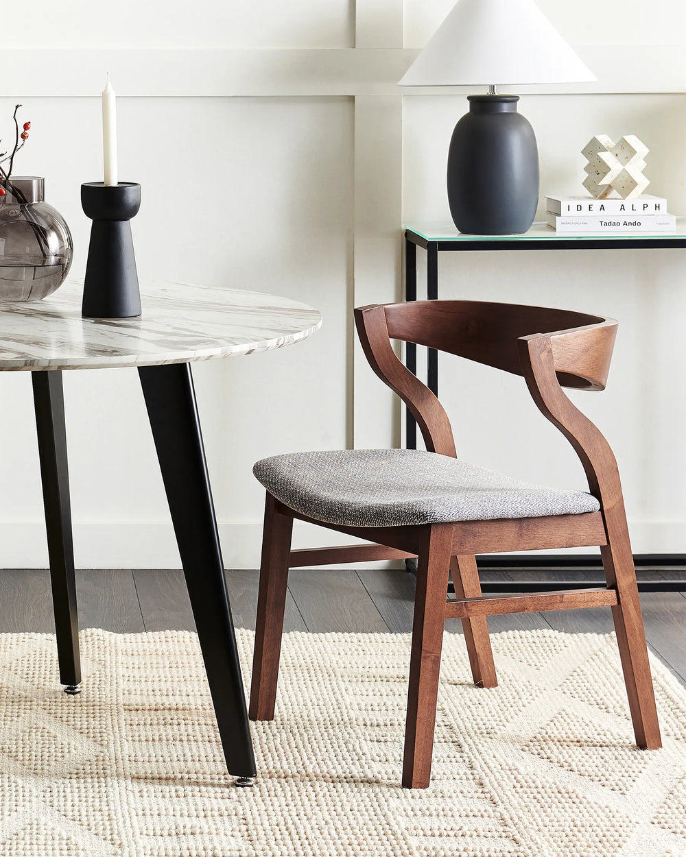 Walnut dining chairs with soft grey textured upholstery styled beside a marble dining table in a refined modern interior featuring neutral tones, black accents, sculptural décor, and cozy contemporary styling.