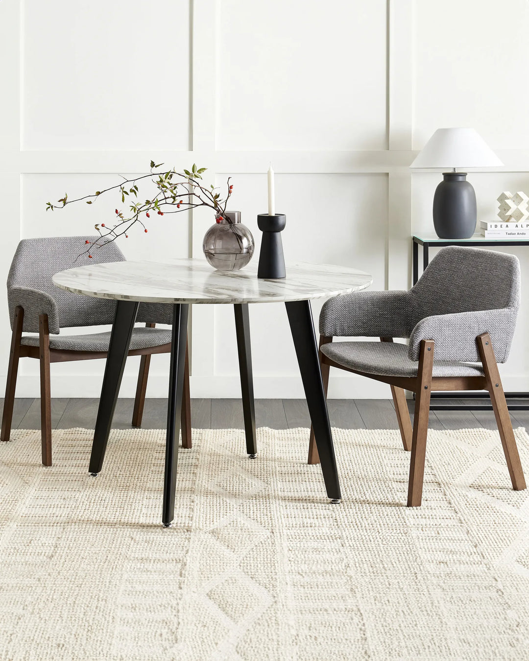 Grey armchairs with walnut frames around a round marble dining table in a bright, modern dining room with minimalist décor.
