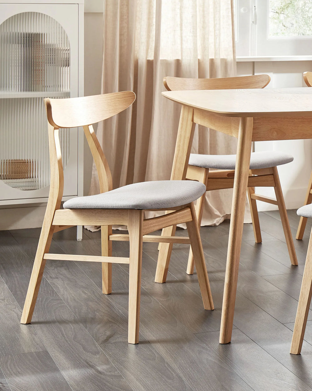 Light wood dining chairs with curved backrests and upholstered seats styled around a wooden dining table in a bright modern dining room.