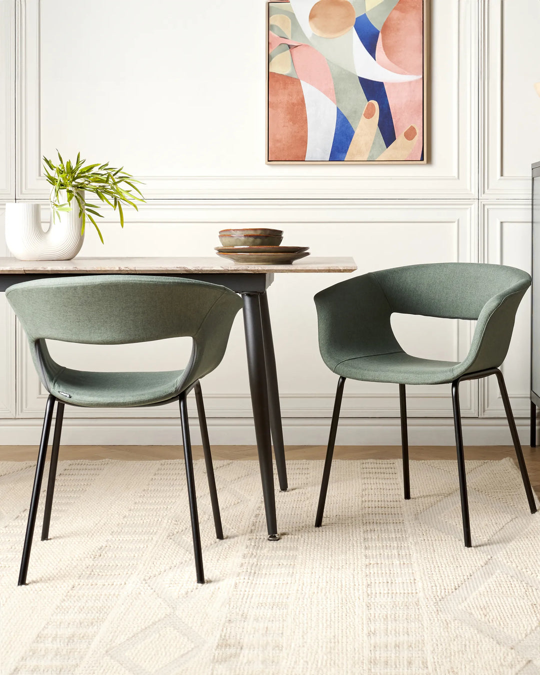 Dark green fabric dining chairs with curved low backrests and black metal legs arranged around a dining table in a contemporary dining space with modern décor.
